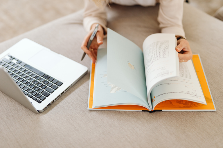 Eine Person schreibt in ein Buch. Daneben steht ein Laptop