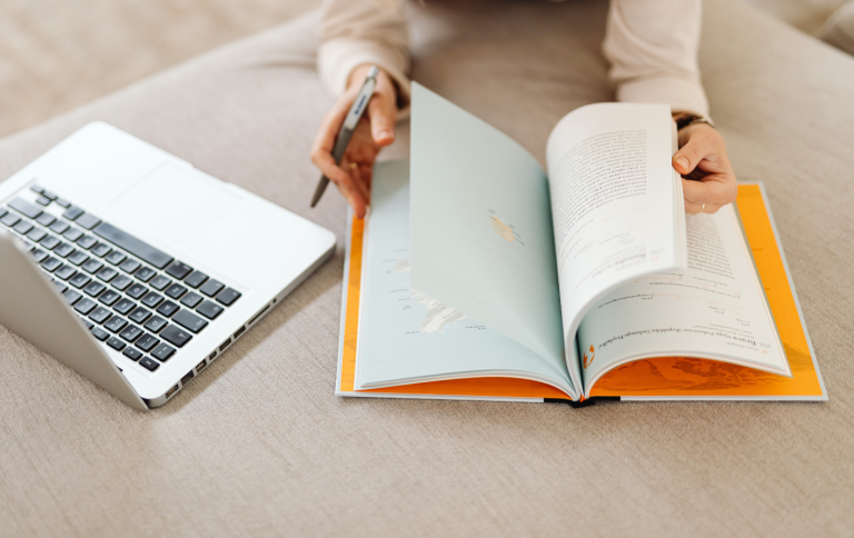 Eine Person schreibt in ein Buch. Daneben steht ein Laptop