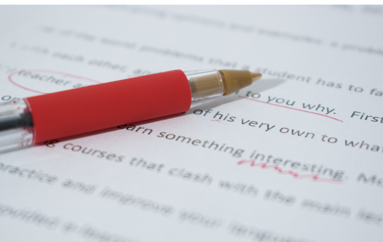 ein roter Stift liegt auf einem beschriebenen Papier. Der abgebildete Text wird korrigiert